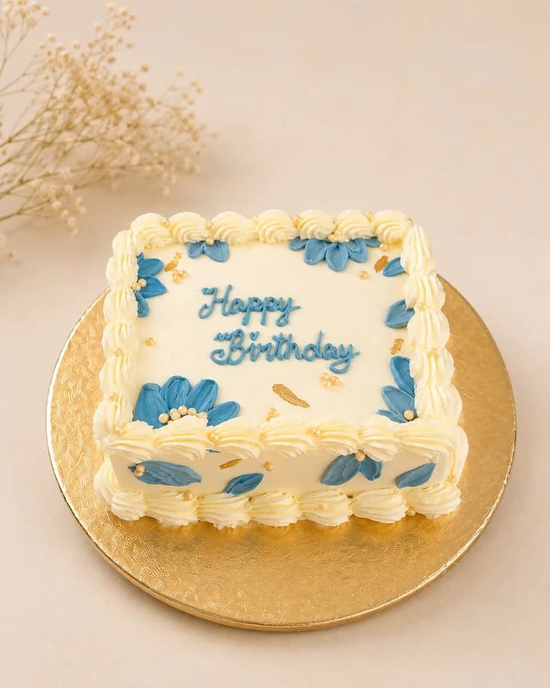 Square cake with blue piped flowers and gold pearls