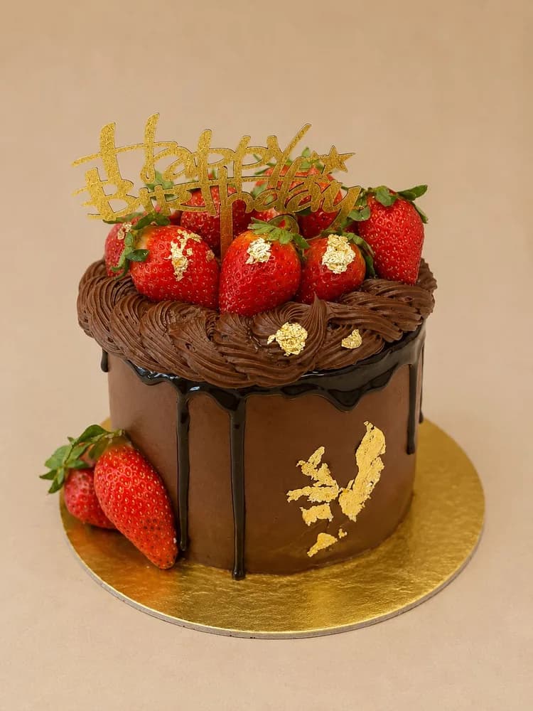 Chocolate drip cake topped with strawberries and gold leaf